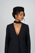 A woman wearing a black woll pillbox hat and a black open-front blazer 