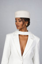A woman wearing a white wool pillbox hat with a signature CÈGLÈ logo and white blazer