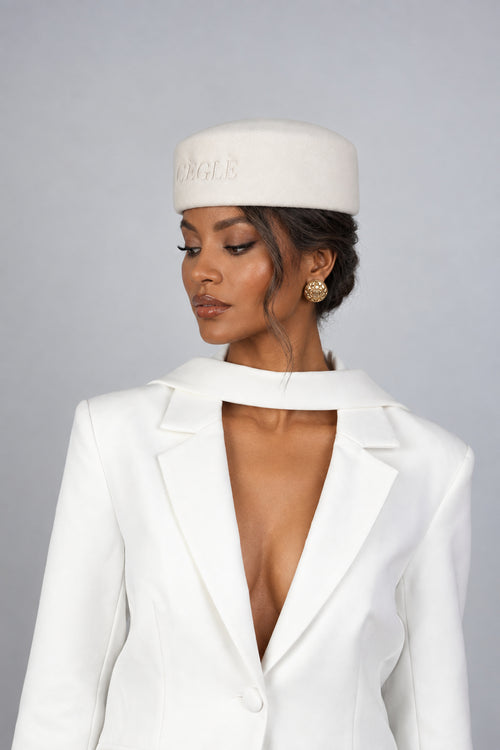 A woman wearing a white wool pillbox hat with a signature CÈGLÈ logo and white blazer