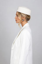 A woman wearing a white wool pillbox hat with a signature CÈGLÈ logo and structured white blazer, elegant classic old money style look