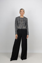 A model wearing a black and white CÈGLÈ tweed cropped jacket with front buttons paired with wide-leg black pants.