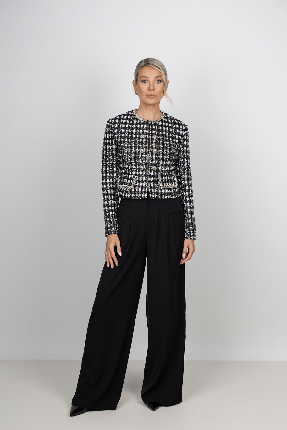 A model wearing a black and white CÈGLÈ tweed cropped jacket with front buttons paired with wide-leg black pants.