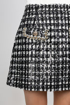 Close-up of a black and white tweed mini skirt with a decorative beaded pocket trim and a gold-tone button