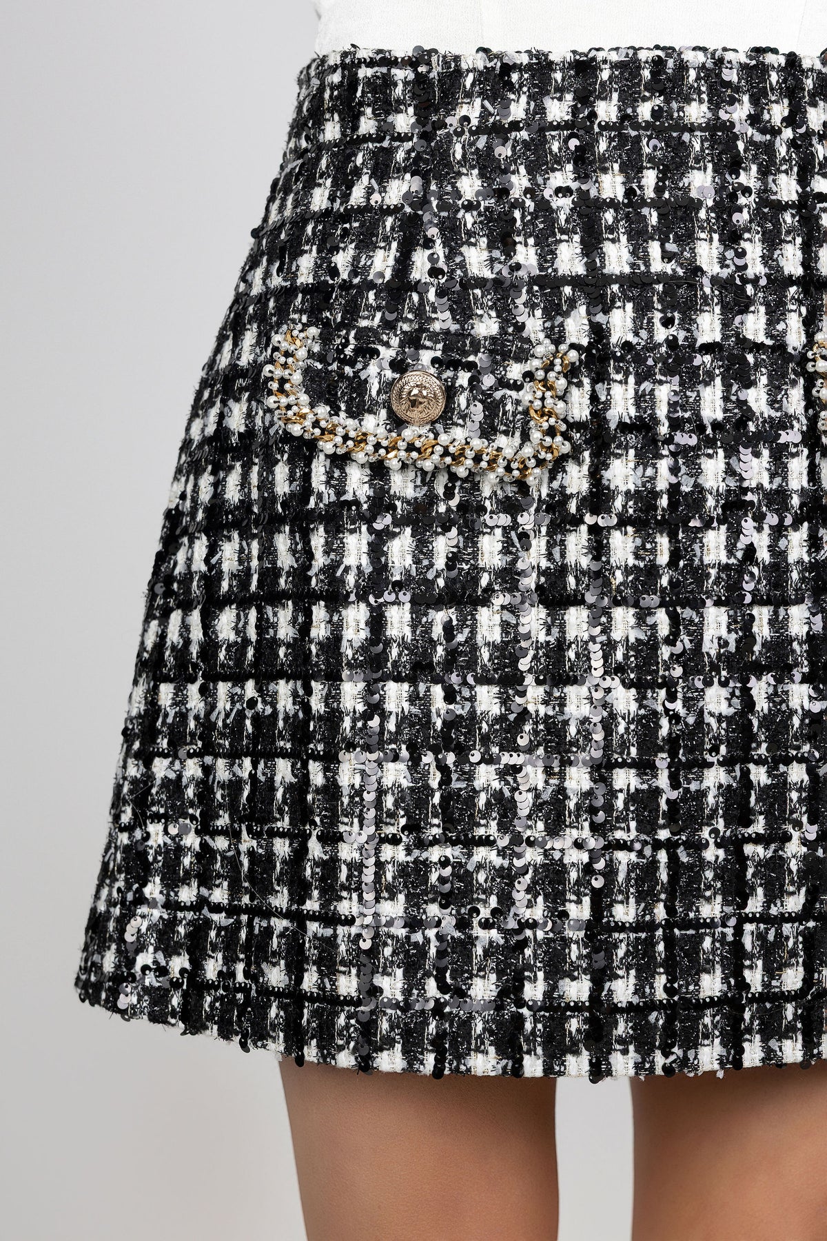 Close-up of a black and white tweed mini skirt with a decorative beaded pocket trim and a gold-tone button