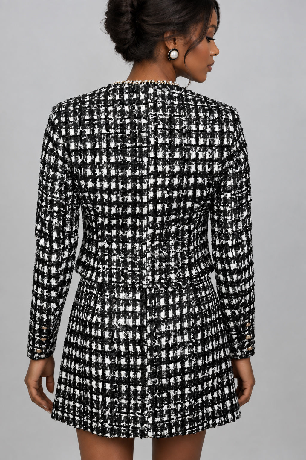 A woman shown from the back wearing a black and white tweed blazer and skirt set 
