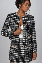 A woman in a black and white tweed jacket and matching mini skirt set with pearl trim and gold-tone buttons