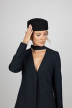 A woman wearing a black wool pillbox hat with a signature CÈGLÈ logo 