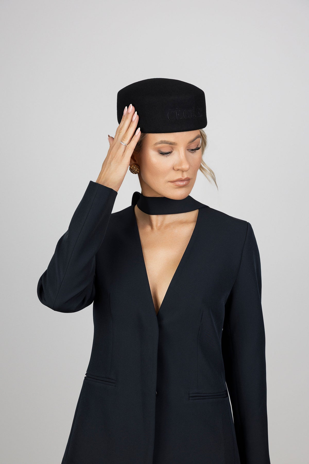 A woman wearing a black wool pillbox hat with a signature CÈGLÈ logo 