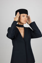 A woman wearing a black woll pillbox hathat and a black long-sleeve blazer with a deep V-neck and choker collar