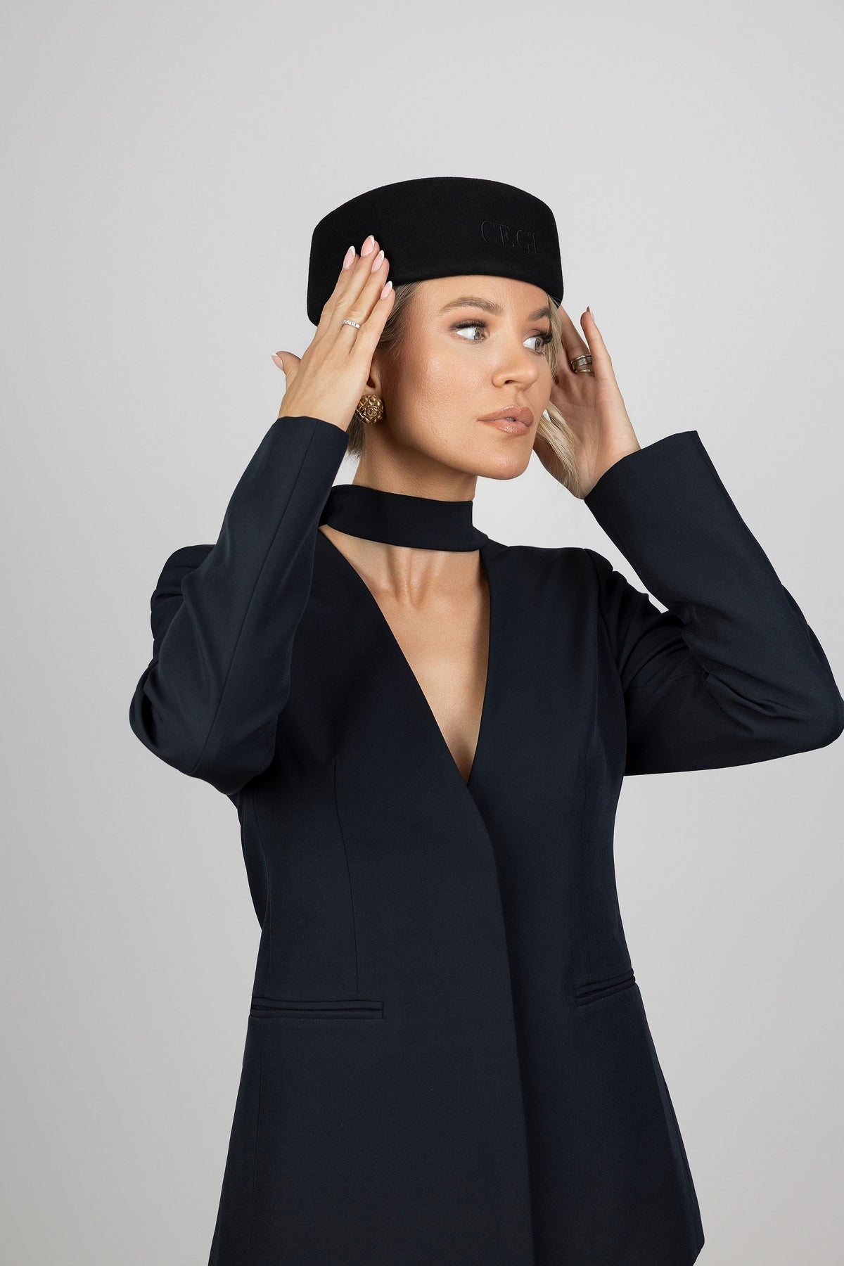 A woman wearing a black woll pillbox hathat and a black long-sleeve blazer with a deep V-neck and choker collar