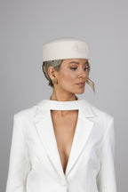 A woman wearing a white wool pillbox hat with a signature CÈGLÈ logo and white blazer